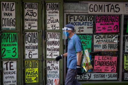 Un hombre camina frente a una vitrina de la que cuelgan carteles con precios de alimentos el 15 de octubre de 2020, en Caracas (EFE/ Miguel Guti&#233;rrez)